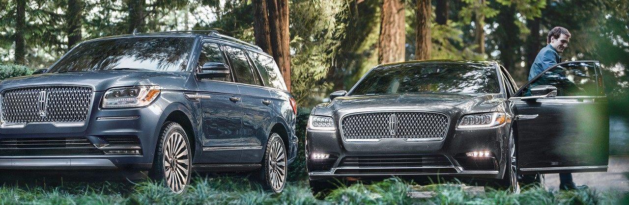Luxury Lincoln SUV and sedan parked in a wooded area, emphasizing elegance and style.