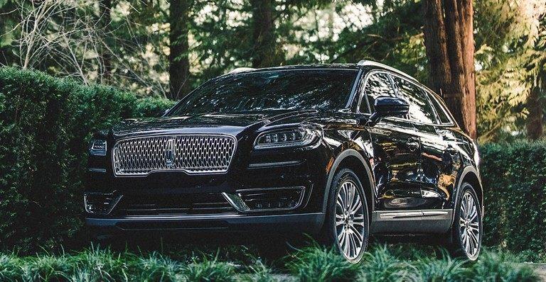 Luxury black SUV parked in a lush forest setting, highlighting sleek design and elegance.