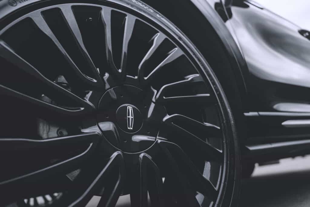 Close-up of a sleek black car wheel with an emblem, featuring stylish spokes and a shiny finish.