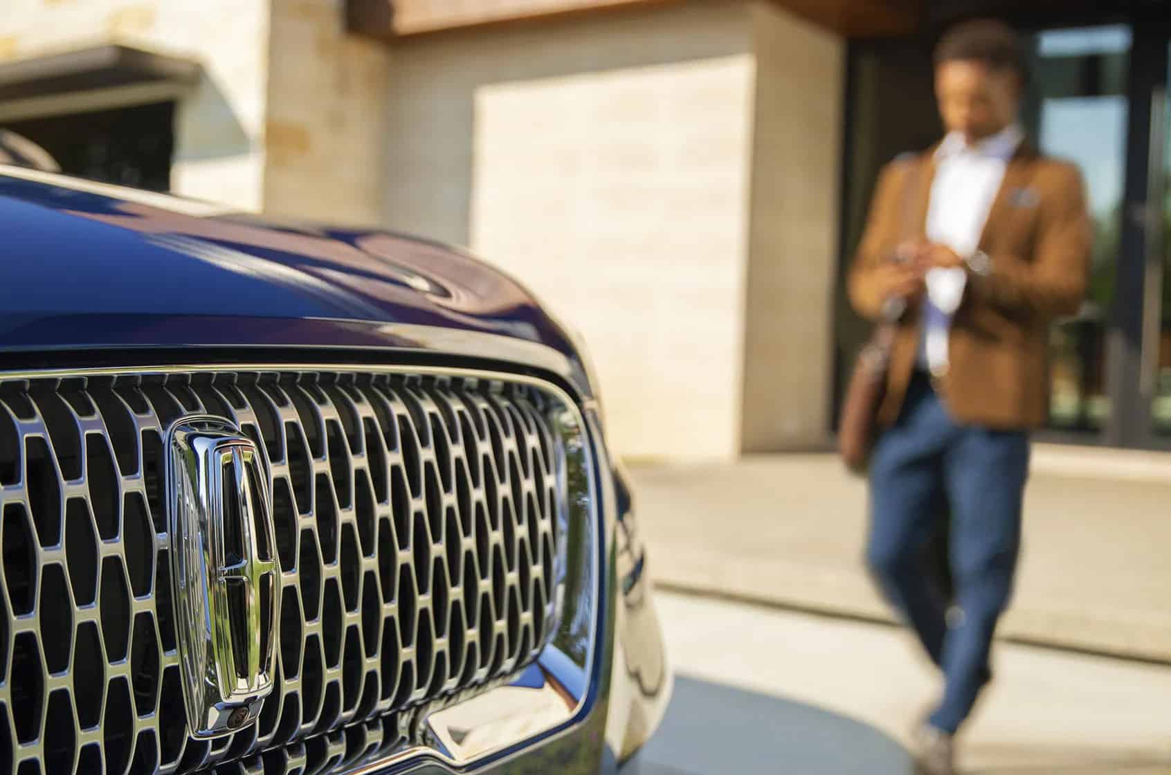 Close-up of a car grille with a blurred person in the background, creating a sense of modern sophistication.