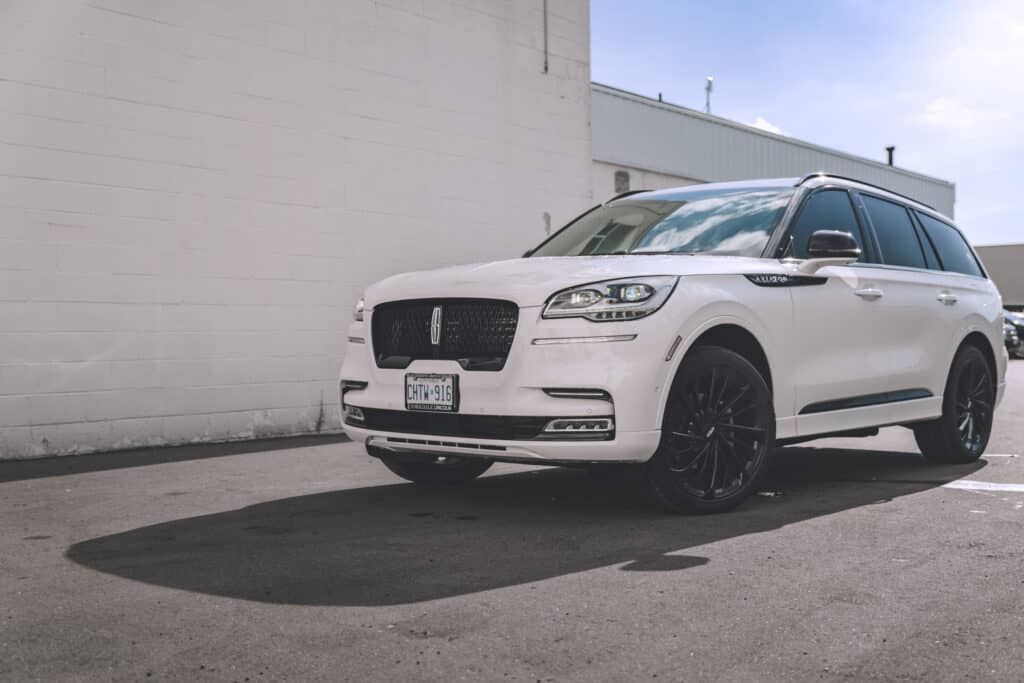 White Lincoln SUV parked in a sunlit urban lot, showcasing sleek design and black wheels.