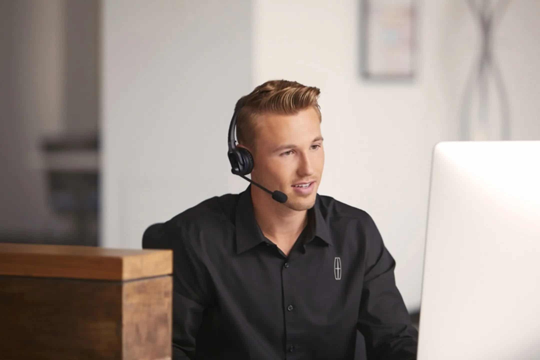 A man wearing a headset works at a computer, providing customer service support in an office.