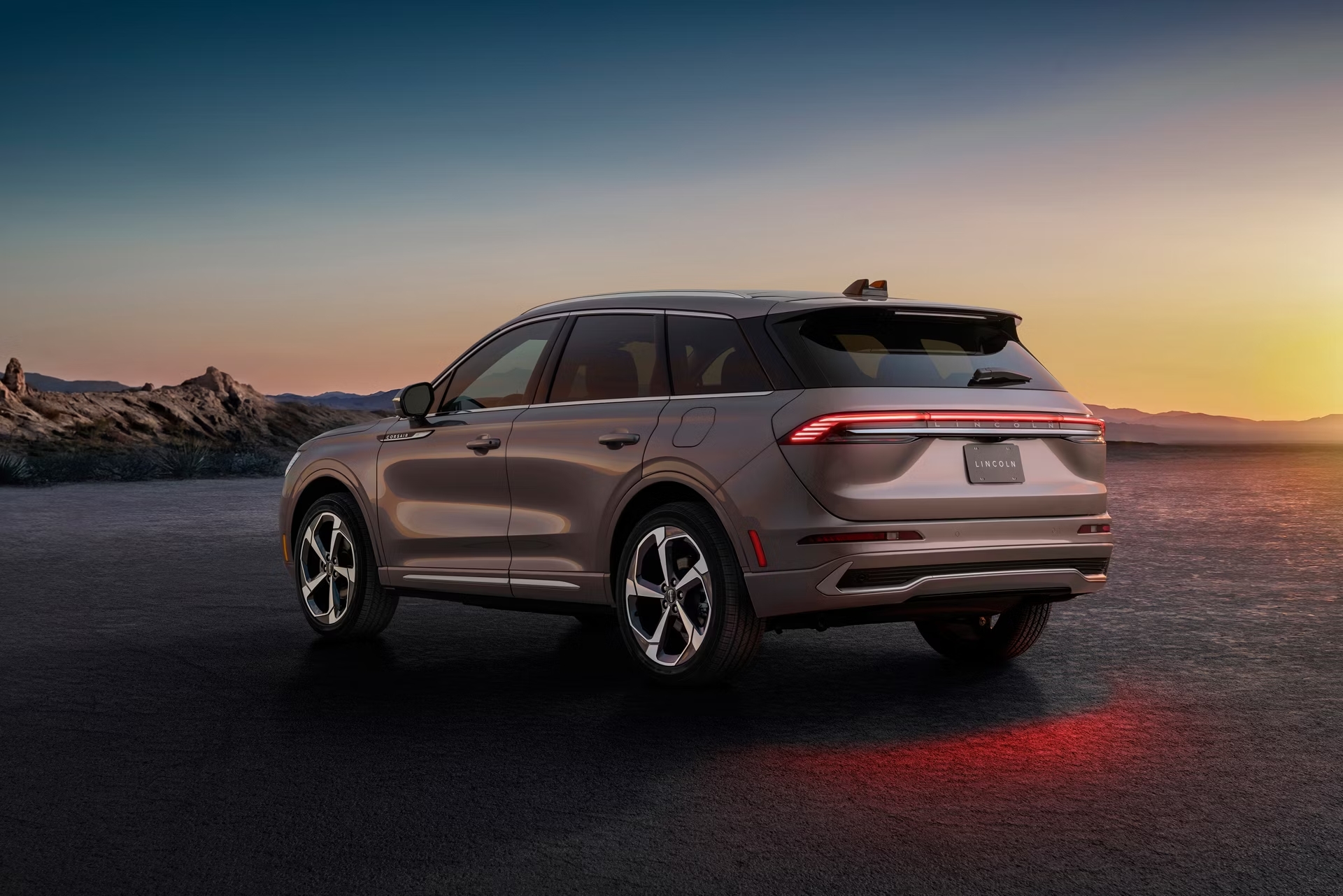 SUV parked on an open road at sunset, highlighting sleek design and taillights against mountainous backdrop.